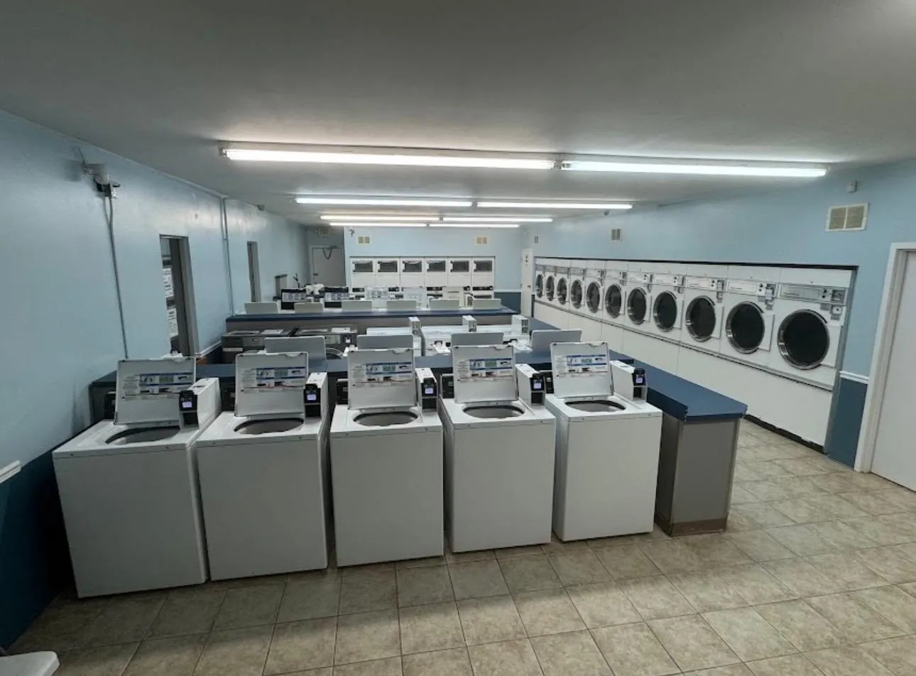 The bright blue main room: a row of top-load washers in front and a long wall of front-load machines on the right.