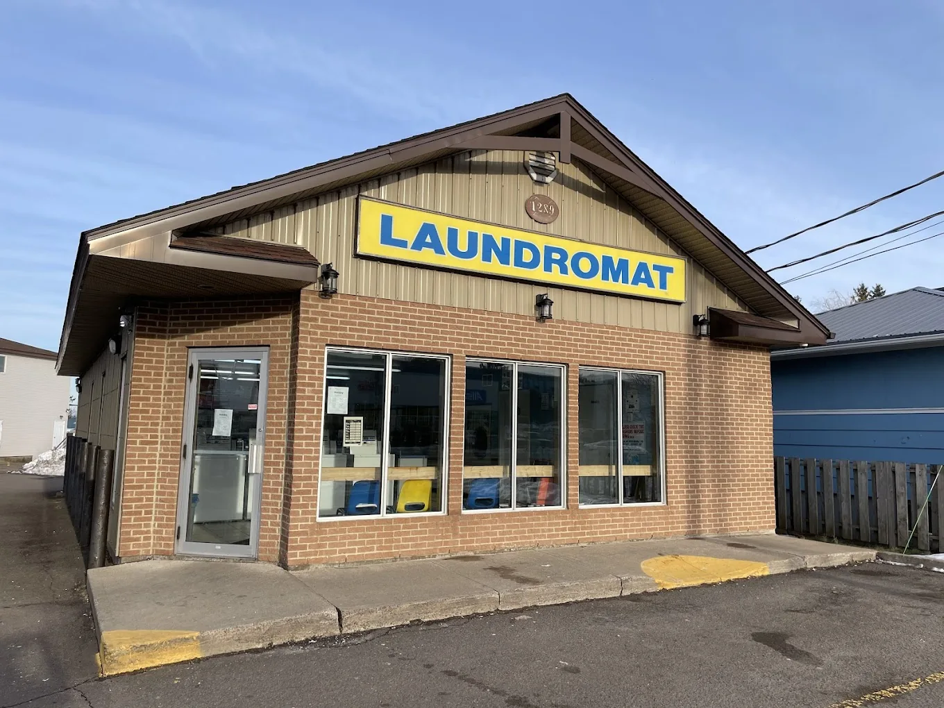 Mountain Laundromat on a sunny day: a brick building with a yellow and blue LAUNDROMAT sign, a glass door and big front windows.