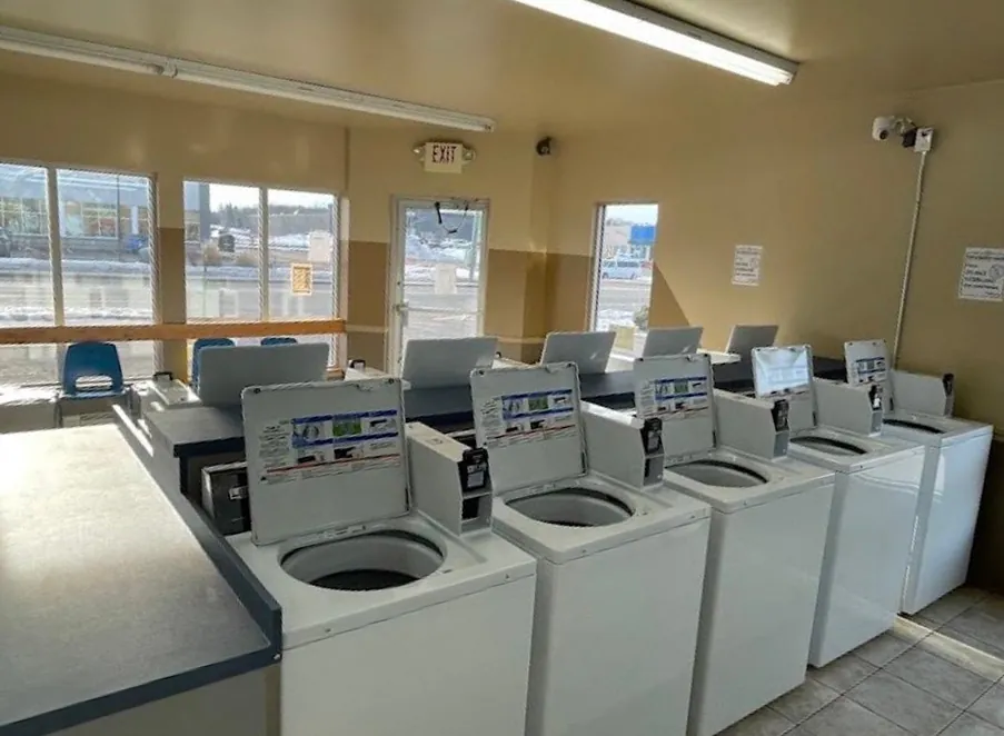 Top-load washers with their lids open, beside big front windows.